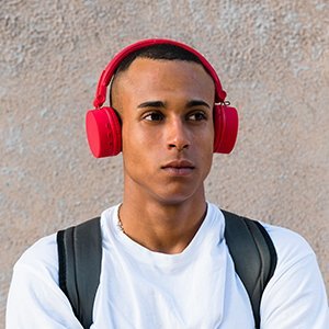 A young man wearing red headphones and a white shirt, standing outdoors against a textured wall.