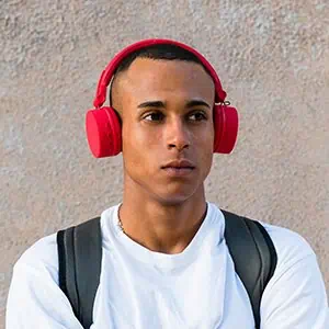 A young man wearing red headphones and a white shirt, standing outdoors against a textured wall.