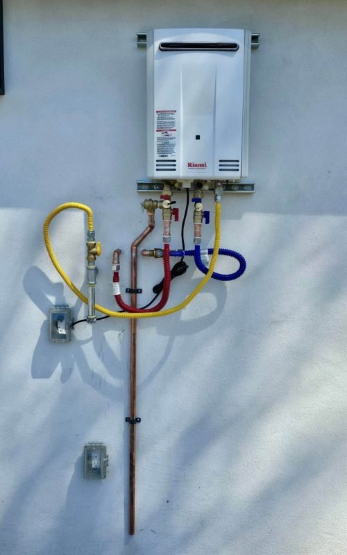 Water heater with connected yellow, red, and blue pipes on a wall.