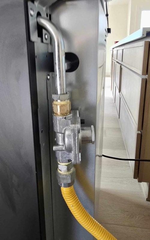Gas line connection with brass fittings and yellow flexible pipe.